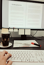 im Vordergrund eine Tastatur mit Hand, im Hintergrund ein Bildschirm mit einem Grabungsbericht